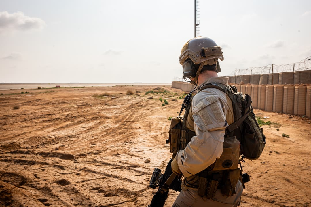 Person i ørkenterreng ved et inngjerdet anlegg.